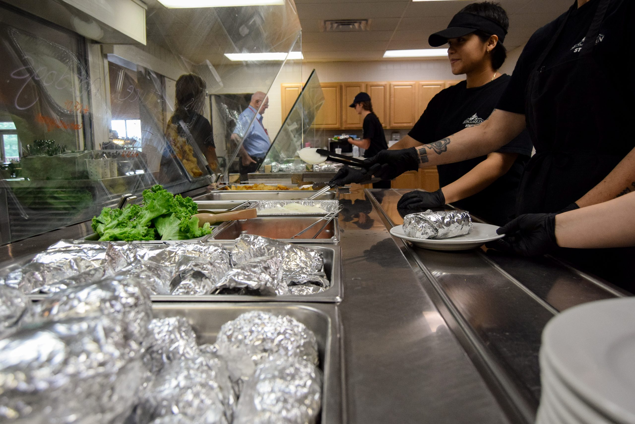 foodservice workers serve foil-wrapped sandwiches and other food from a buffet line